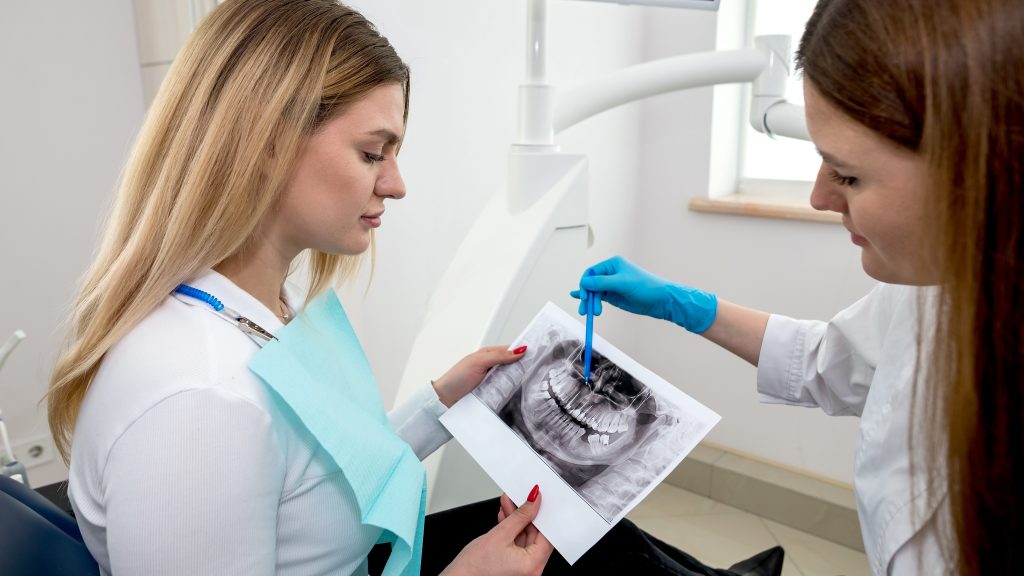 The dentist shows the x-ray image to the patient. People, medicine, dentistry, technology and healthcare concept.