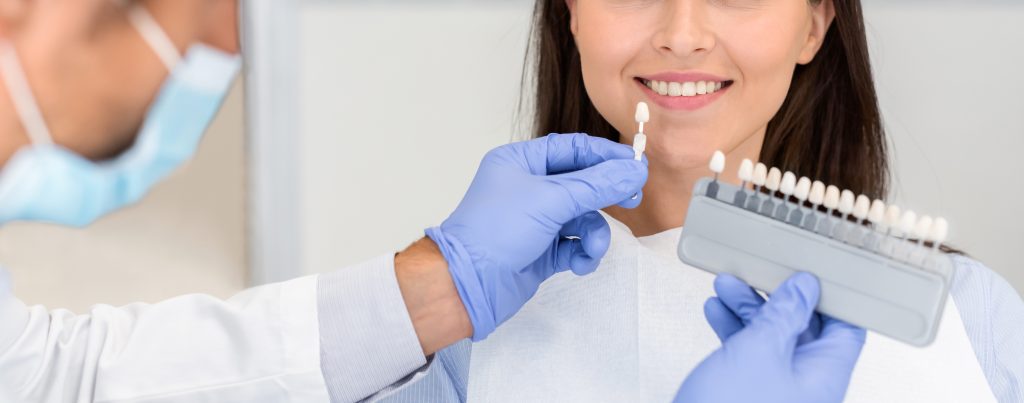 Dentist applying sample from tooth scale to smiling patient teeth