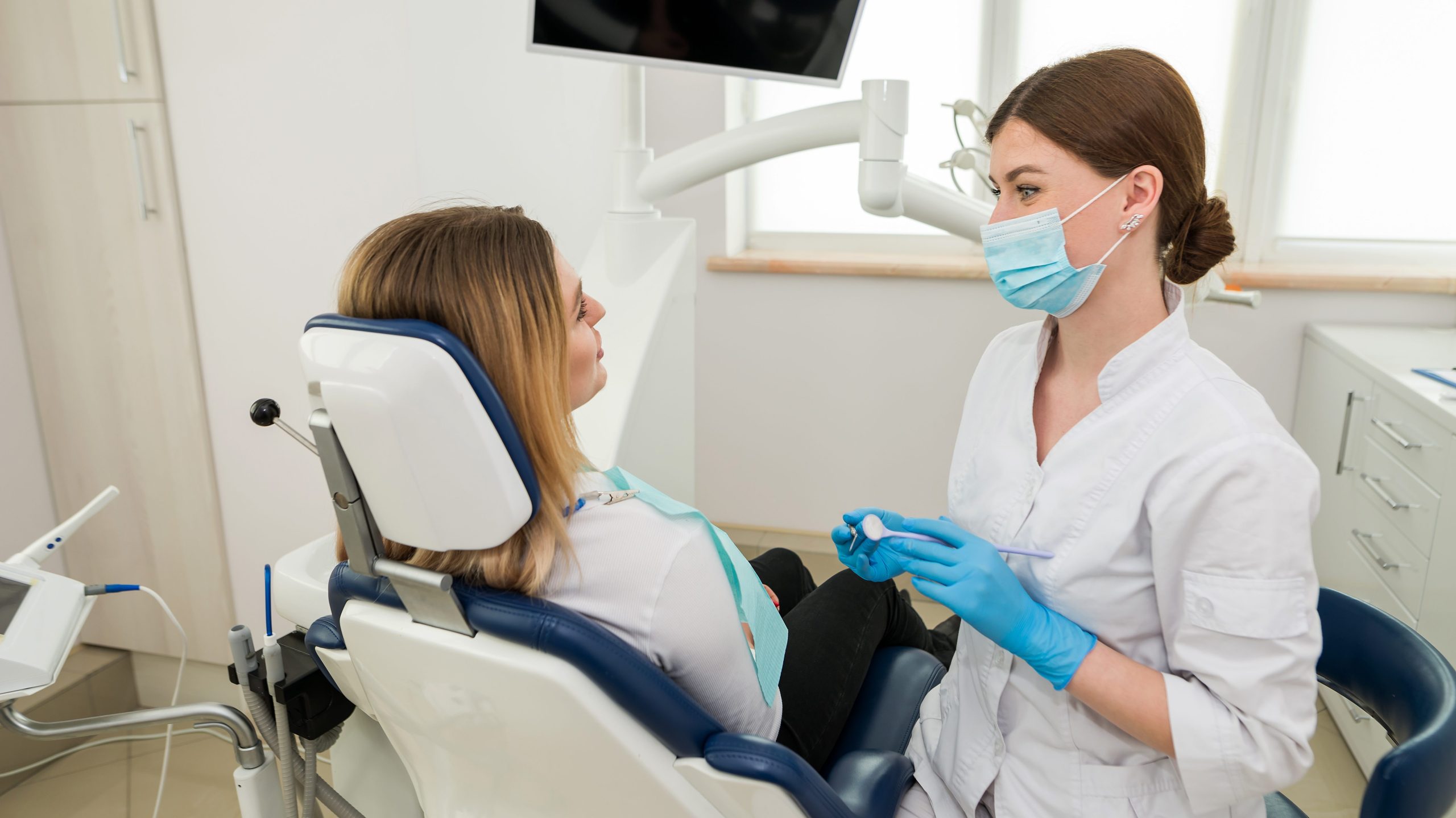 A beautiful female dentist is talking to a patient while sitting in a chair.