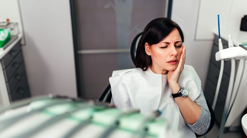 Woman suffering from toothache sitting at dental chair at dentis