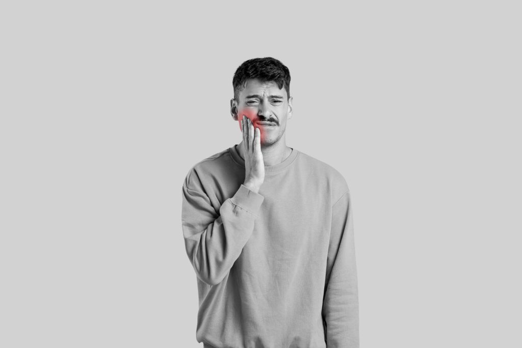 Man rubbing cheek in pain on gray background