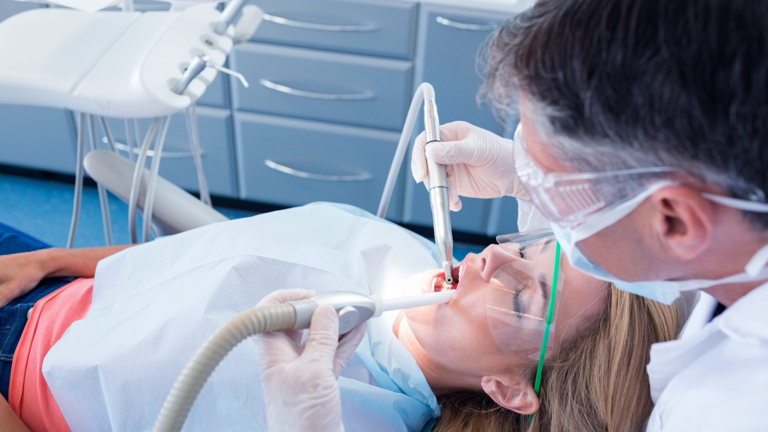 Dentist examining his patient with a suction hose at the dental clinic