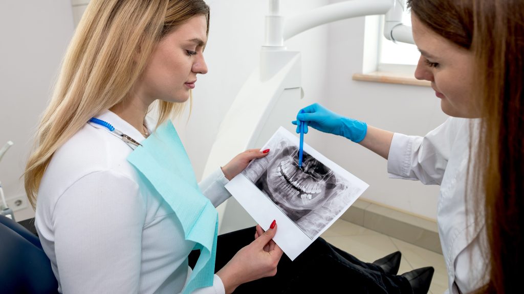 The dentist shows the x-ray image to the patient. People, medicine, dentistry, technology and healthcare concept.