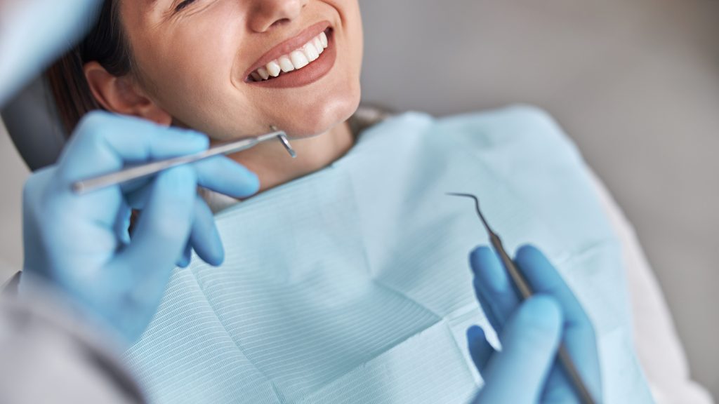 Cheerful positive dentist and client in dentistry. Female patient at dental procedure, doctor using dental instruments in modern dental clinic