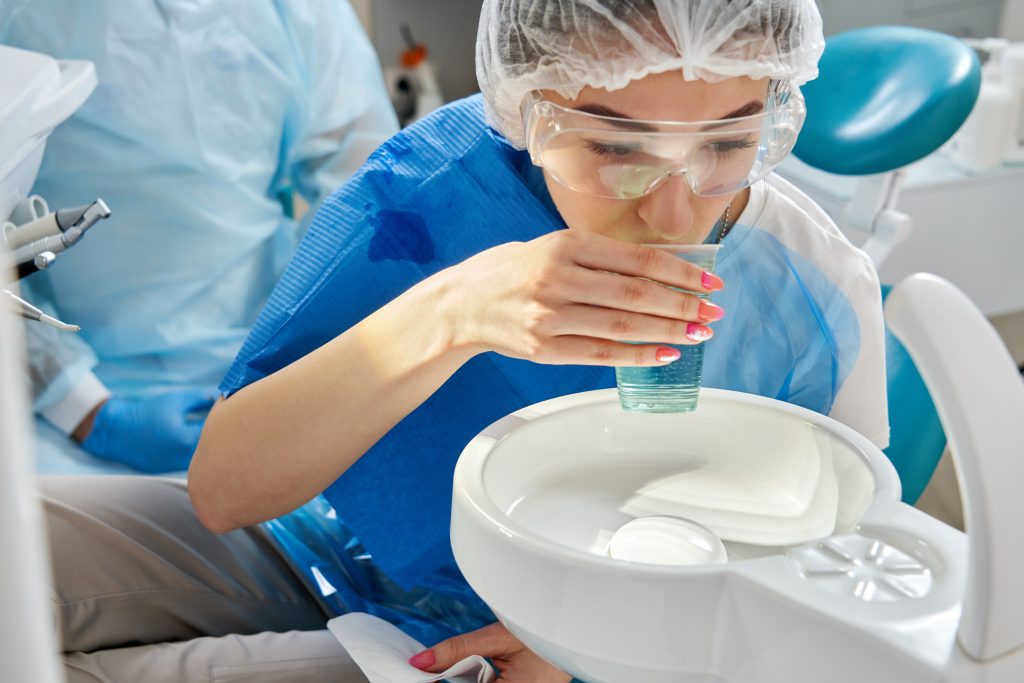Woman patient sitting in dental chair with glass of water, rinsing teeth after treatment, visit to doctor dentist