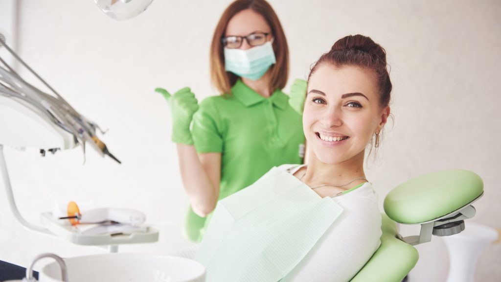 A young woman is satisfied with the work of the dentist and holds up her thumb